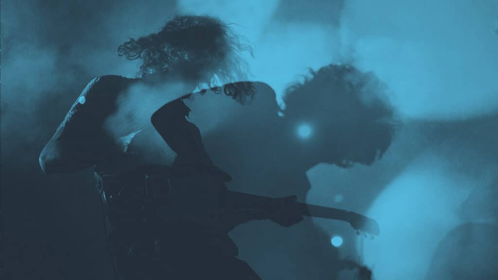 Shadowy image of a man performing on a guitar with a blue overlay.